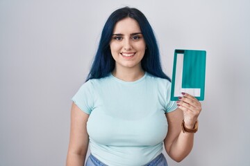 Young modern girl with blue hair holding l sign for new driver looking positive and happy standing and smiling with a confident smile showing teeth