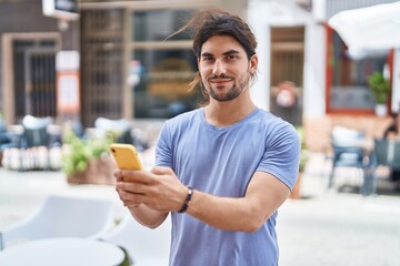 Naklejka premium Young hispanic man smiling confident using smartphone at street