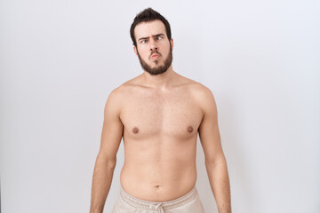 Fototapeta premium Young hispanic man standing shirtless over white background making fish face with lips, crazy and comical gesture. funny expression.