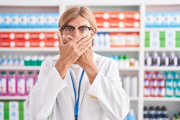 Caucasian man with mustache working at pharmacy drugstore shocked covering mouth with hands for...