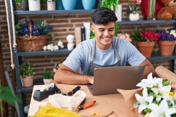 Young hispanic man florist smiling confident using laptop at flower shop