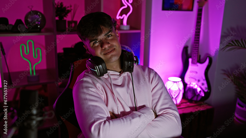 Sticker Cheeky young hispanic man, a master streamer, confidently sporting headphones, smiling with crossed arms, chilling in his cozy gaming room at night, surrounded by technology.