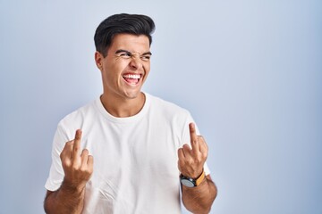 Hispanic man standing over blue background showing middle finger doing fuck you bad expression, provocation and rude attitude. screaming excited