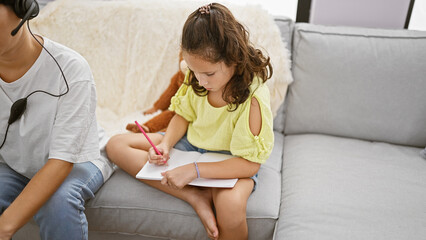 Mother and daughter enjoying family love, sitting together on the living room sofa, working online and drawing in a notebook at home