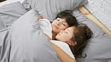 Lying together in their cozy room, a mother and daughter share a loving hug before drifting off to...