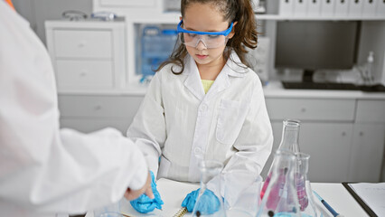Two scientists in safety glasses engrossed in medical research, meticulously taking notes at the...