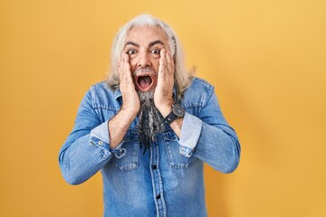 Middle age man with grey hair standing over yellow background afraid and shocked, surprise and...
