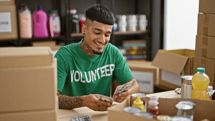 Confident young latin man volunteer, smiling while counting dollars at charity center, making a...