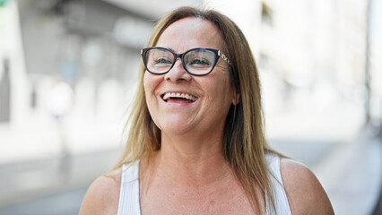 Middle age hispanic woman wearing glasses looking to the side smiling at street