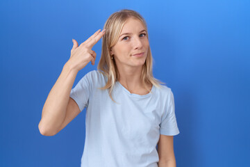 Fototapeta premium Young caucasian woman wearing casual blue t shirt shooting and killing oneself pointing hand and fingers to head like gun, suicide gesture.