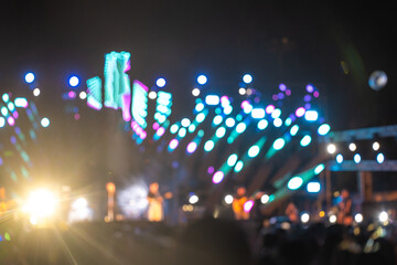 Amid vibrant nightlife a concert festival takes center stage and unrecognizable crowd cheers in front of brilliantly illuminated stage. lens flare captures energy and excitement of music event.
