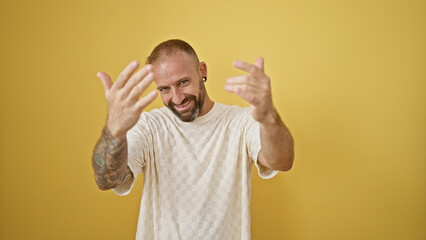 Fototapeta premium Happy young man, exuding confidence, flashing a cool smile and coming gesture with hands isolated on a vibrant yellow background