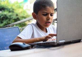 Little boy sitting at table using laptop for online class in Grade 1, Child studying on laptop from home for distance learning online education, School boy children lifestyle concept
