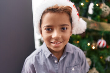 Adorable hispanic boy smiling confident standing by christmas tree at home