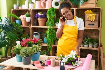 Fototapeta premium African american woman florist smiling confident talking on smartphone at flower shop