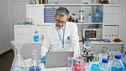 Serious grey-haired young hispanic man a scientist, engrossed in his work while sitting at...