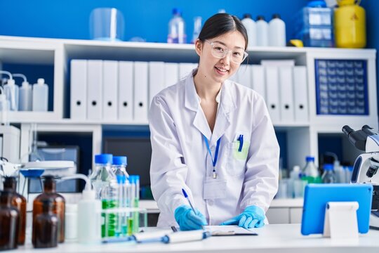 Chinese woman scientist writing on document using touchpad at laboratory