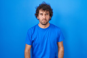 Fototapeta na wymiar Hispanic young man standing over blue background skeptic and nervous, frowning upset because of problem. negative person.
