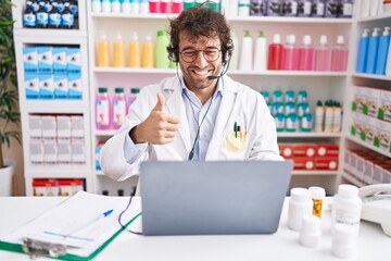 Hispanic young man working at pharmacy drugstore working with laptop smiling happy and positive,...