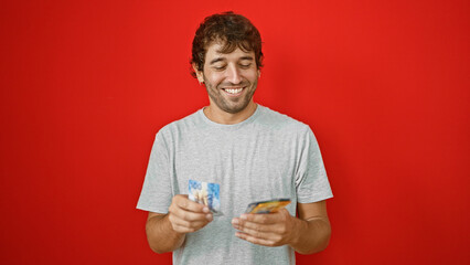 Young man counting swiss francs banknotes smiling over isolated red background