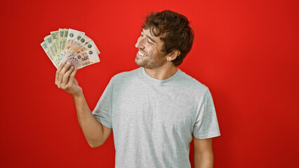 Young, smiling man confidently holding and counting his wealth in argentine pesos banknotes,...