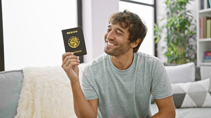 Joyful young hispanic man confidently smiling, holding his mexican passport, sitting casually on...