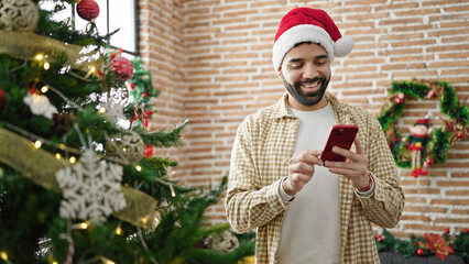 Young hispanic man celebrating christmas using smartphone at home