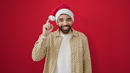 Young hispanic man smiling wearing christmas hat getting an idea over isolated red background