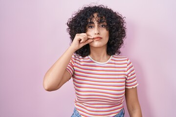 Young middle east woman standing over pink background mouth and lips shut as zip with fingers....