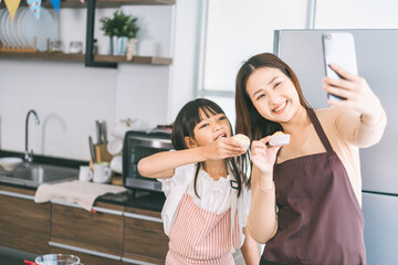 Happy asian family mother and daughter cooking in kitchen selfie with smartphone for social media
