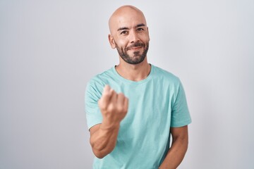 Middle age bald man standing over white background beckoning come here gesture with hand inviting welcoming happy and smiling