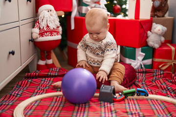 Fototapeta na wymiar Adorable caucasian baby playing with train toy sitting on floor by christmas gifts at home
