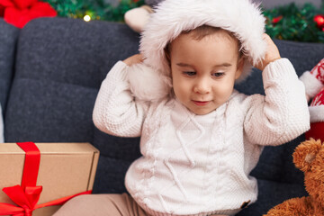 Adorable hispanic toddler wearing christmas hat sitting on sofa at home