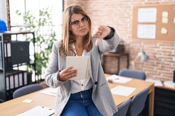 Young hispanic woman working at the office wearing glasses looking unhappy and angry showing...