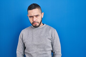 Hispanic man standing over blue background skeptic and nervous, frowning upset because of problem. negative person.