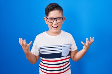 Young hispanic kid standing over blue background celebrating mad and crazy for success with arms...