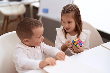 Adorable girl and boy playing with color puzzle cube sitting on table at kindergarten - Powered by Adobe