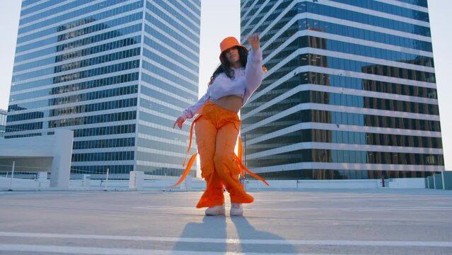 Cool fashionable artist city street dance performance on roof top at sunset. Aggressive talented mixed race woman dancing. Sexy girl performing modern club provocative body moves at urban background