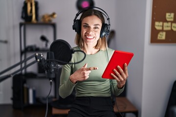 Hispanic woman singing song using microphone and tablet smiling happy pointing with hand and finger