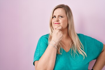 Caucasian plus size woman standing over pink background looking confident at the camera smiling...