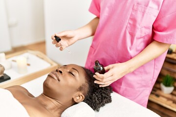 Obraz na płótnie Canvas African american woman lying on massage table having facial treatment at beauty salon