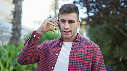 Portrait of a cool, relaxed hispanic guy, seriously engrossed in a call on his smartphone, immersed...