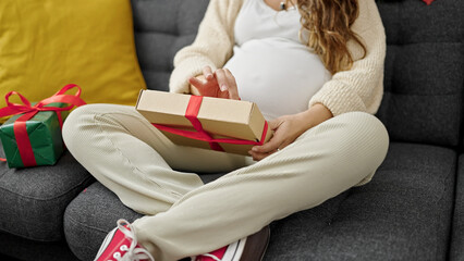 Young pregnant woman touching belly holding christmas gift at home