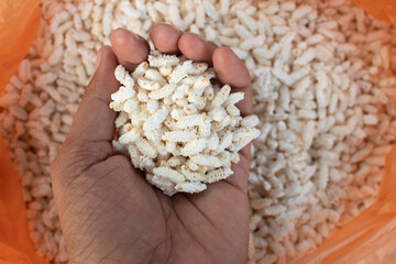 kheel or murmura in hand on background of orange plastic bag, India.