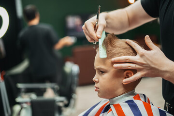 The master hairdresser works with a hair scissors and cuts the boys. Medium frame view, hand held...