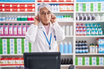 Middle age woman with tattoos working at pharmacy drugstore covering ears with fingers with annoyed expression for the noise of loud music. deaf concept.