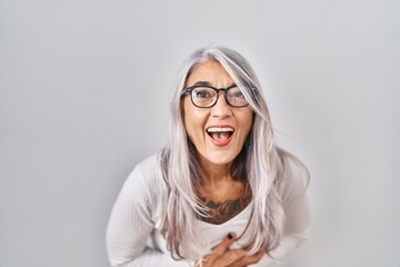 Middle age woman with grey hair standing over white background smiling and laughing hard out loud because funny crazy joke with hands on body.