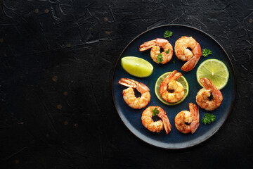 Shrimps, overhead flat lay shot on a black background with copy space. Grilled shrimp with lime, spicy seafood dish