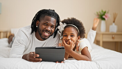 African american father and daughter watching video on touchpad lying on bed at bedroom