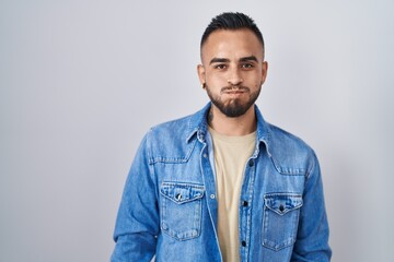 Young hispanic man standing over isolated background puffing cheeks with funny face. mouth inflated...